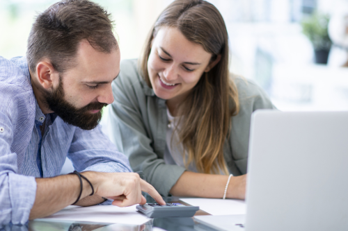 Casal a calcular valores com uma calculadora e portátil sobre a mesa